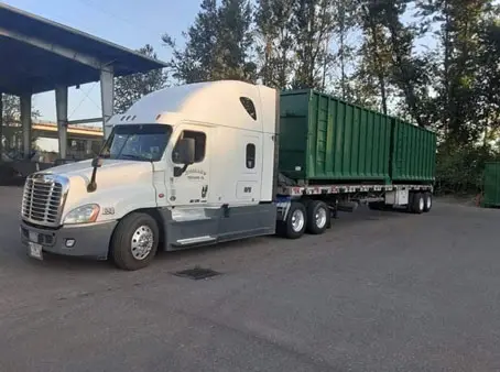 White semi-truck hauling green dumpsters.